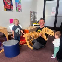 Adults and children with dinosaur model in playroom.