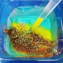 Plastic spoon in a container with colorful liquids and glitter.