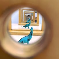Blue toy dinosaur viewed through tube in repeated mirror reflection.