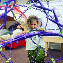 Child playing with a purple geometric climbing structure indoors.