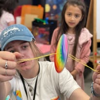 Person playing with a colorful spinning disc toy, child watching in the background.
