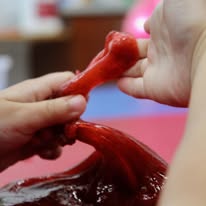 Hands stretching red slime on a blurred colorful background.