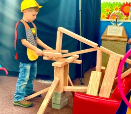 Child in hard hat playing with wooden blocks in a colorful space.