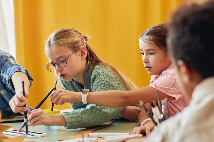 Children sitting at a table, painting and working on crafts with focused expressions.