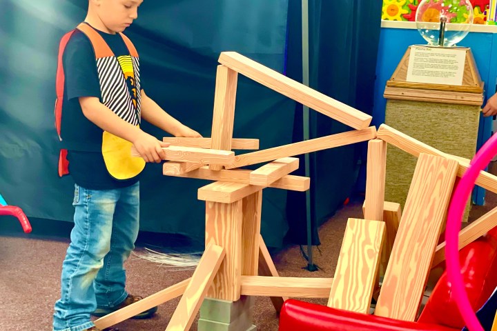 Child wearing a hardhat building with wooden blocks in a play area.