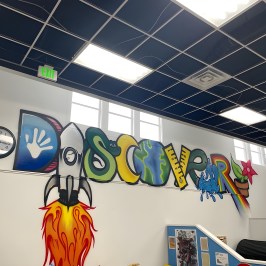 Colorful mural spelling 'DISCOVER' with various themed letters and illustrations on a classroom wall.