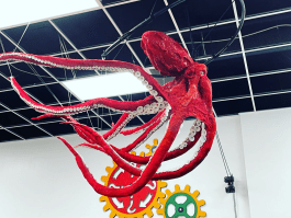Large red octopus sculpture suspended from ceiling with colorful gear decorations in the background.