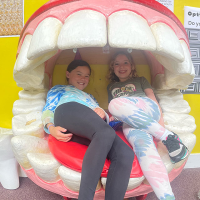 Two kids sitting in a giant mouth sculpture, smiling.