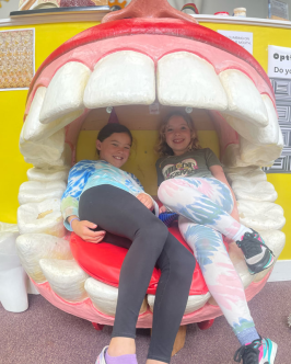 Two kids sitting in a giant mouth sculpture, smiling.