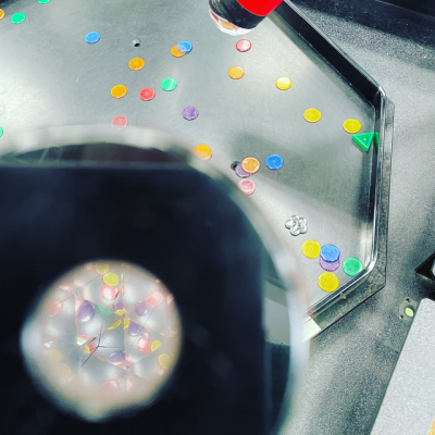 Colorful discs scattered inside a black-framed, octagonal machine with a red handle.