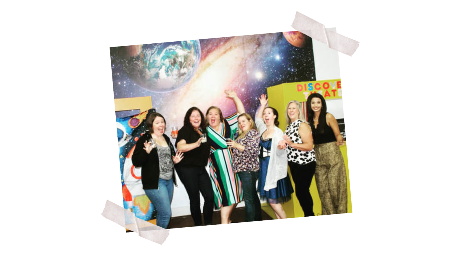 Seven women smiling and posing in front of a space-themed mural.
