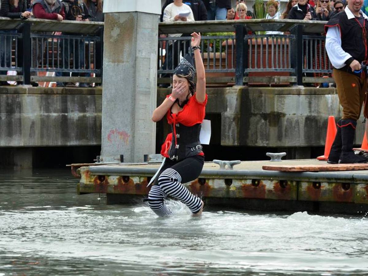Person in pirate costume jumps into water from a dock, covering their mouth.