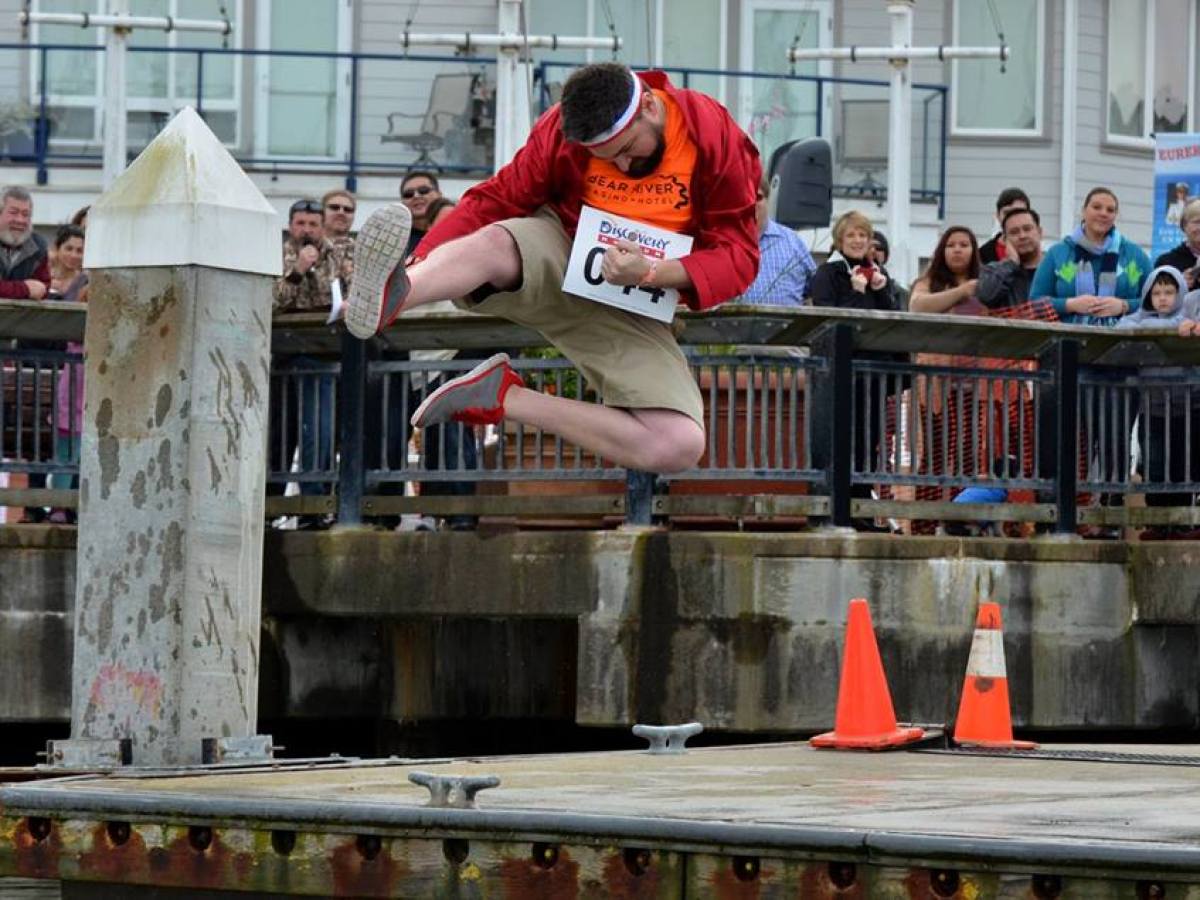 Person in mid-air over a dock, surrounded by an audience, near traffic cones.