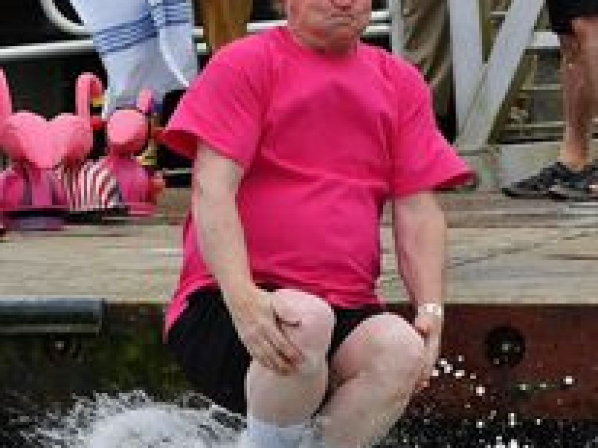 Man in pink shirt jumps into water with knees bent, making a splash.