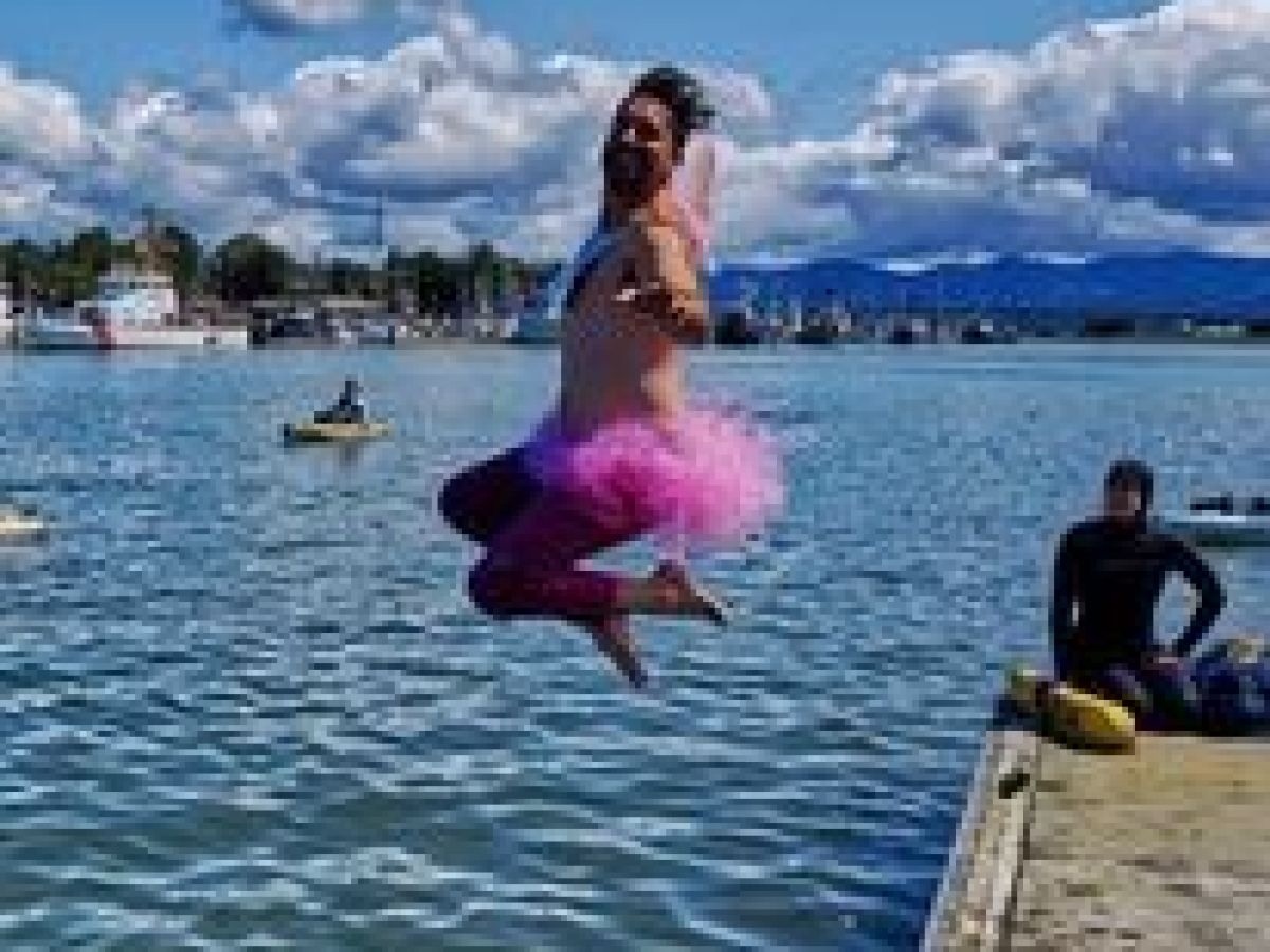 Person in pink tutu jumping into the water, with mountains and clouds in the background.