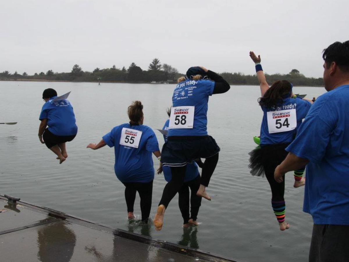 People in blue shirts jumping into a lake from a dock during a group event.