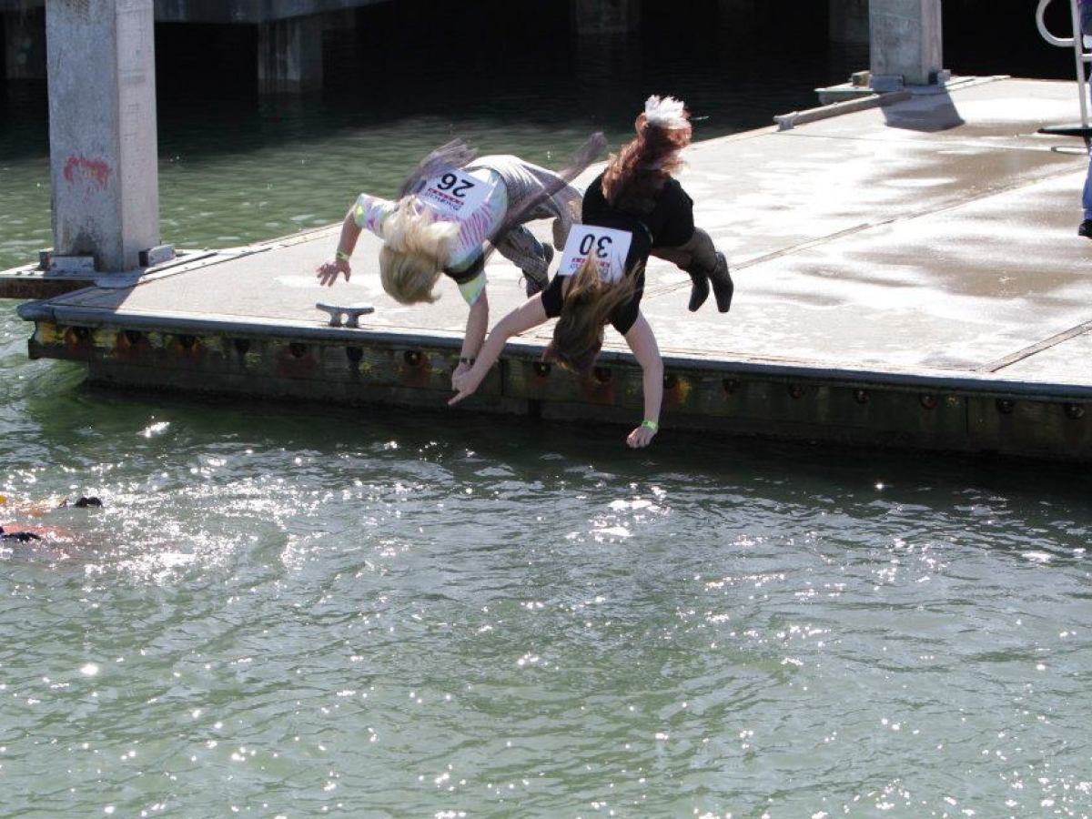 Two people flipping into water from a dock, while another swims nearby.