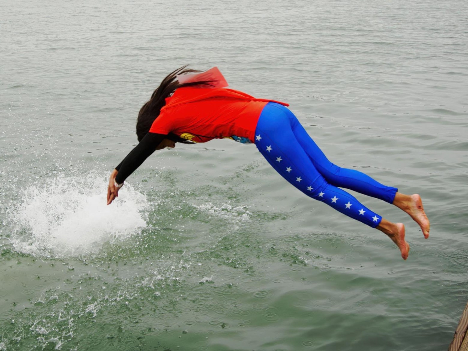 Person in superhero costume diving off a dock into water.