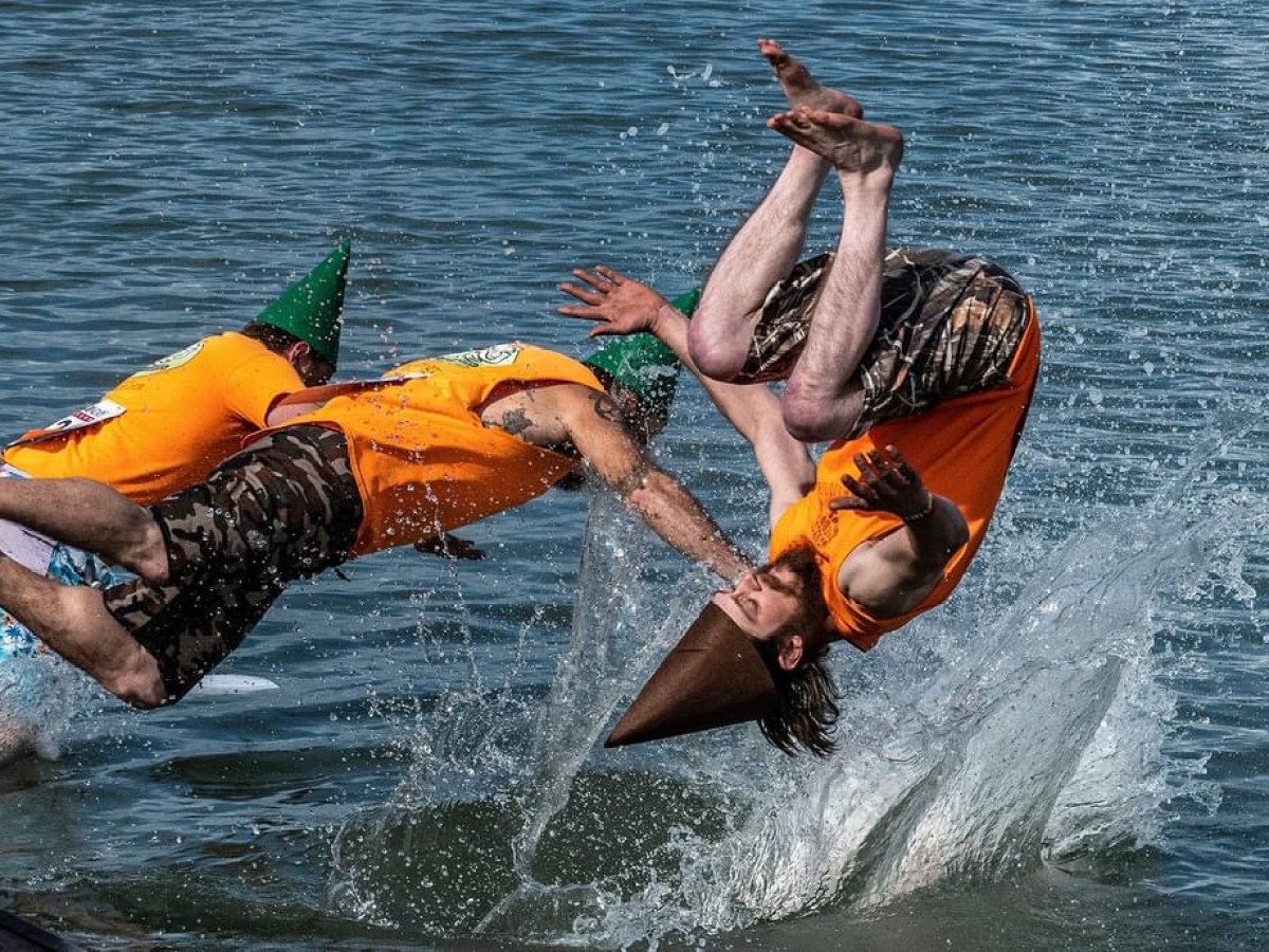 Three people in orange vests perform backflips into water, creating large splashes.