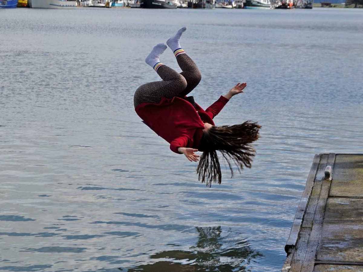 Person in mid-air somersault over water near a dock.