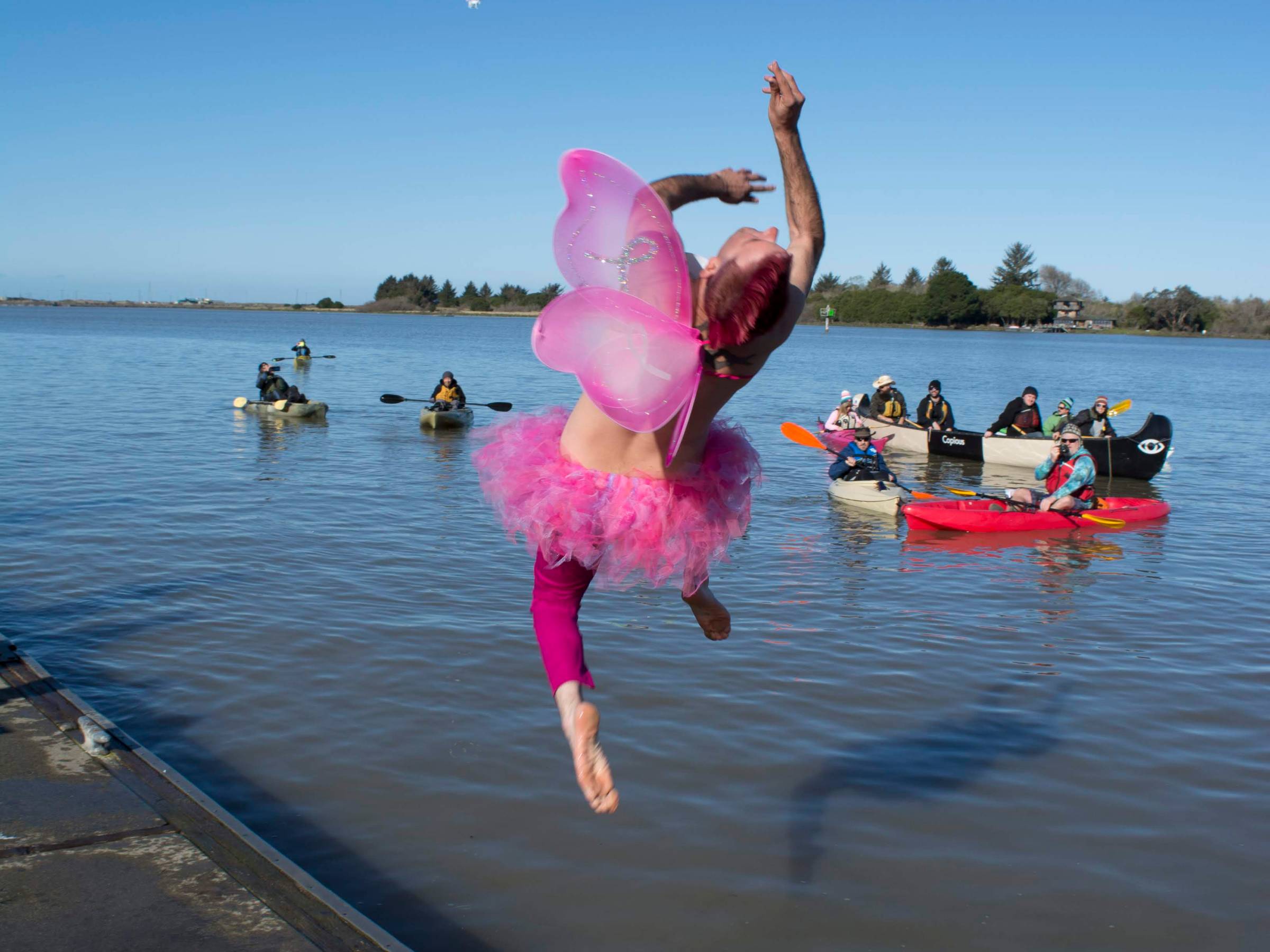 Person in pink fairy costume jumping into a lake, kayakers in the background.