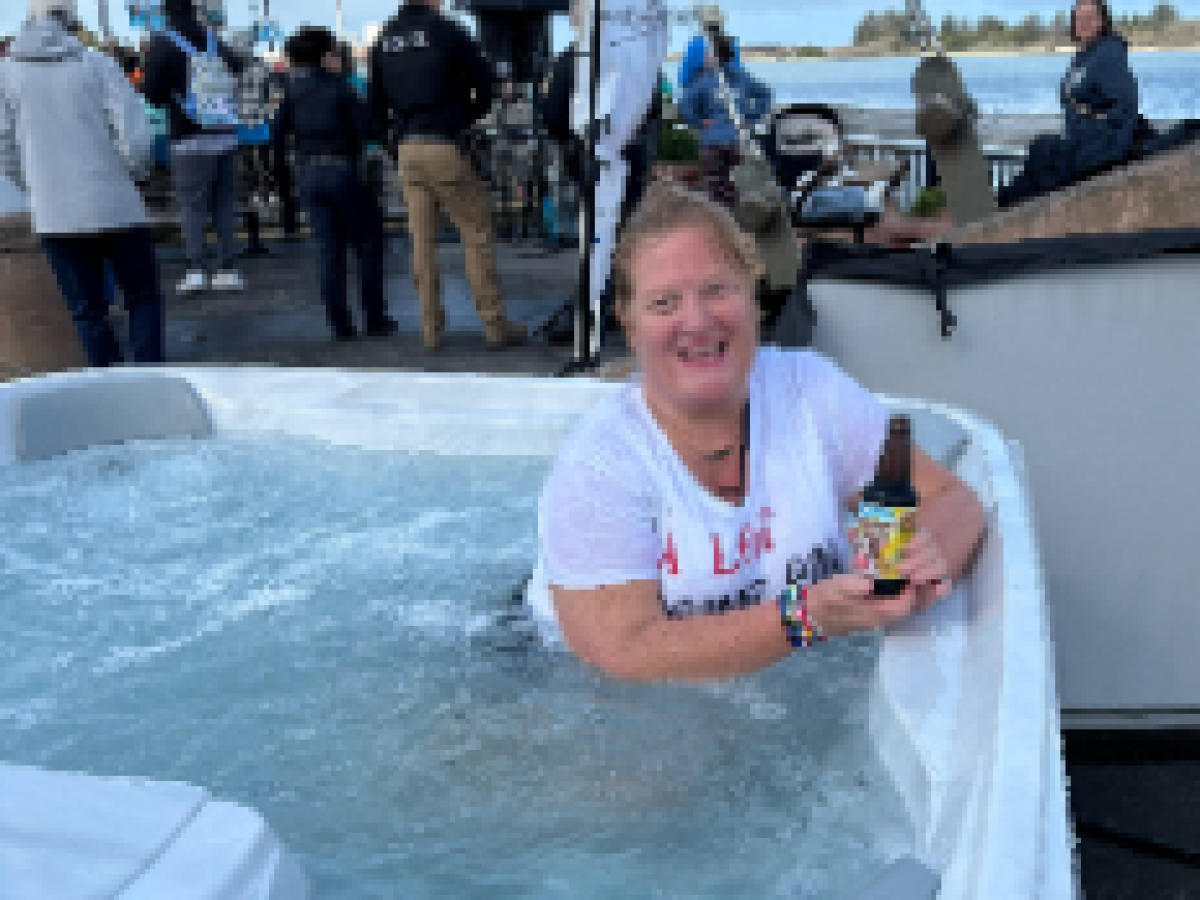 Person in a hot tub on a boat holding a drink, with people and water in the background.